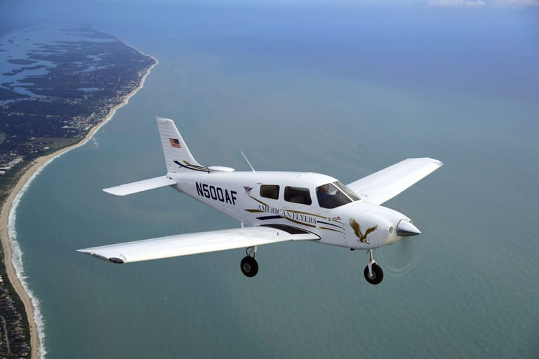 White aircraft flying over turquoise ocean water with coastline visible below